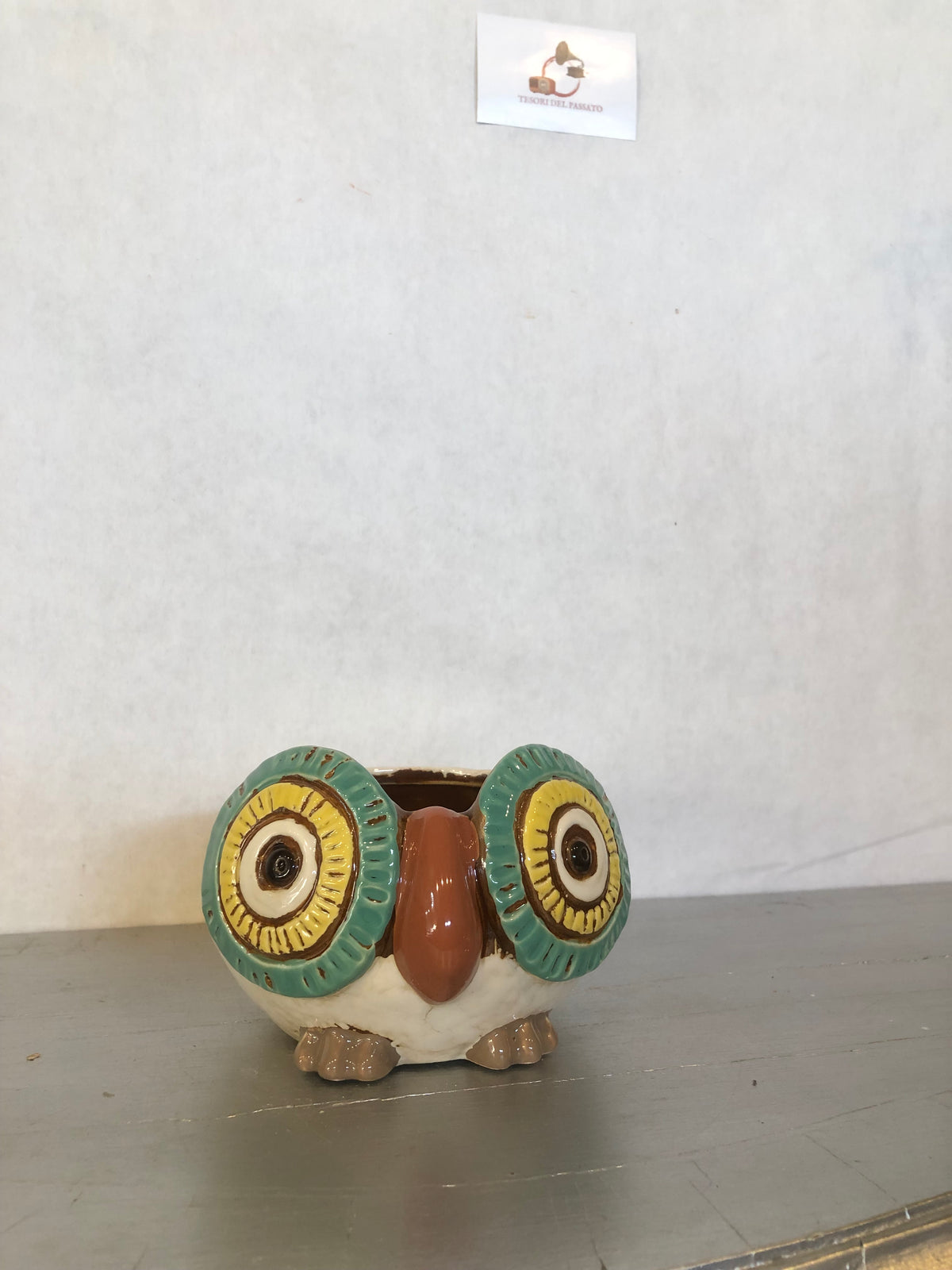 Due civette decorative in ceramica, una con dettagli arancioni e una con dettagli verde acqua e gialli, fotografate su un tavolo in legno in un’atmosfera autunnale e di Halloween, con zucche, foglie e luci calde sullo sfondo.
