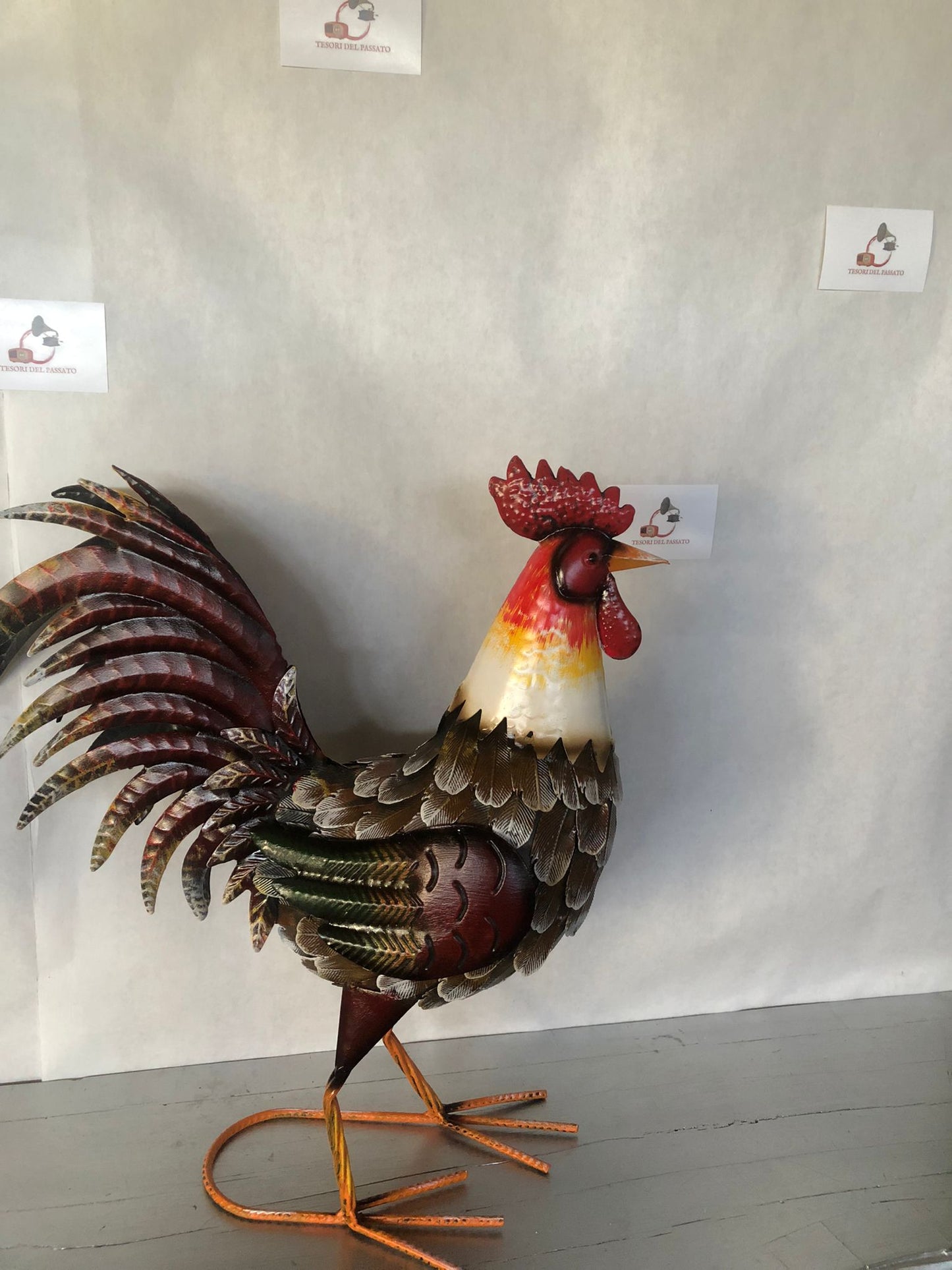 Gallo decorativo in metallo dipinto a mano, ideale per arredare giardino, terrazzo, balcone, portico o ambienti interni in stile rustico e country. Realizzato interamente in metallo con dettagli tridimensionali in rilievo, presenta una ricca lavorazione delle piume e una finitura anticata dai colori vivaci che dona carattere e originalità a qualsiasi spazio. La struttura autoportante garantisce stabilità e permette di posizionarlo facilmente senza necessità di supporti. Perfetto come complemento d'arredo pe