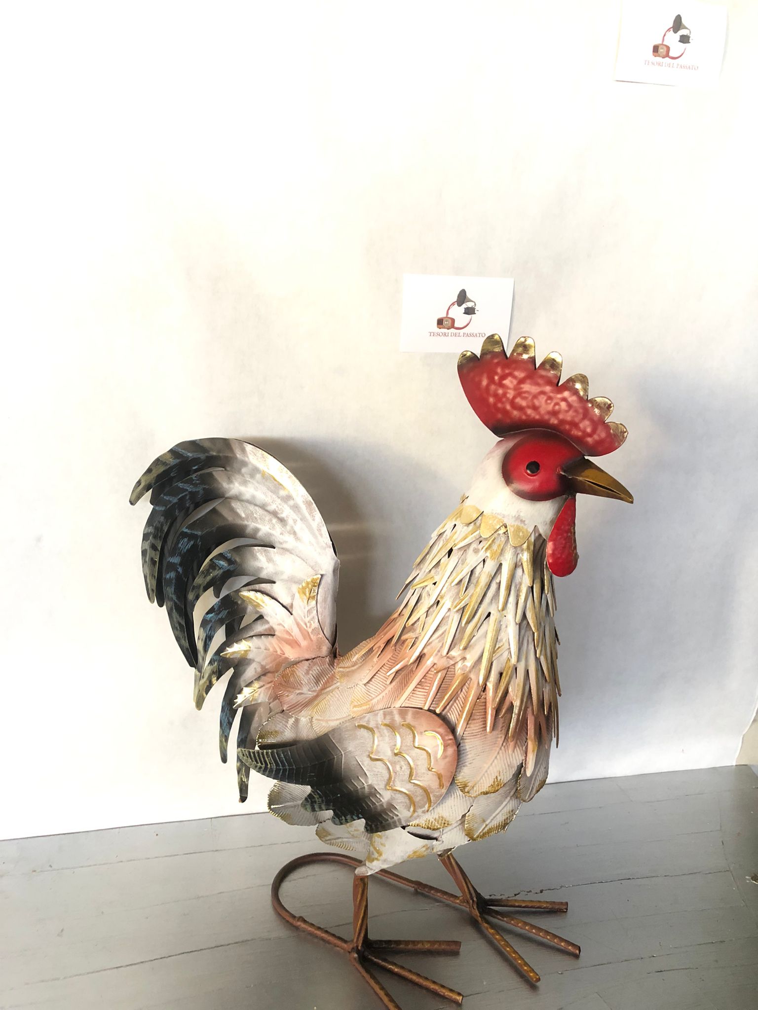 **Gallo decorativo in metallo dipinto a mano, ideale per arredare giardino, terrazzo, balcone, veranda o ambienti interni in stile rustico, country e shabby chic. Realizzato interamente in metallo con lavorazione tridimensionale delle piume, si distingue per la raffinata finitura nei toni del bianco, grigio, nero e oro anticato, impreziosita da cresta e bargigli rossi che donano un aspetto elegante e realistico. La struttura autoportante garantisce stabilità e consente di posizionarlo facilmente su qualsias