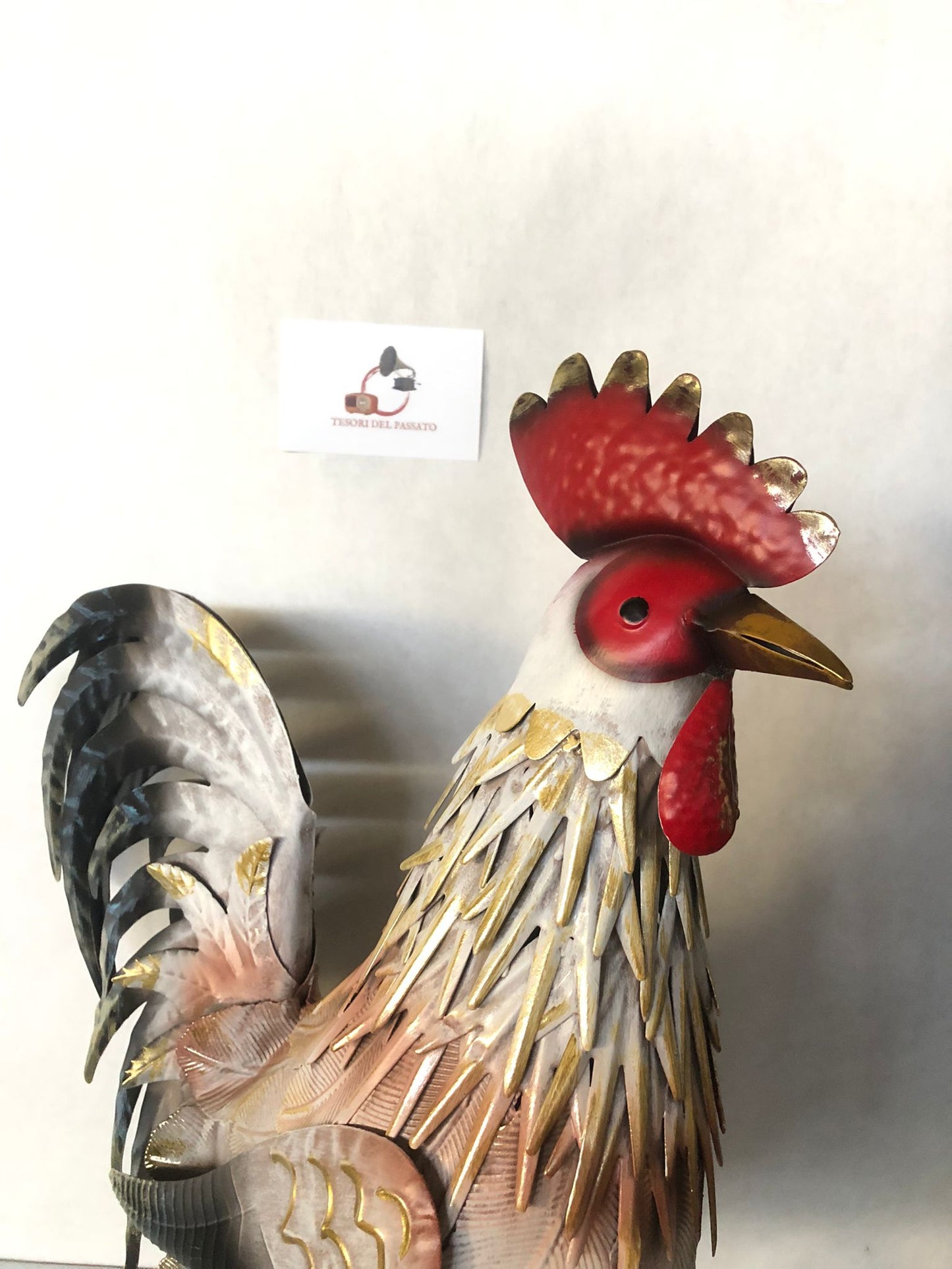 **Gallo decorativo in metallo dipinto a mano, ideale per arredare giardino, terrazzo, balcone, veranda o ambienti interni in stile rustico, country e shabby chic. Realizzato interamente in metallo con lavorazione tridimensionale delle piume, si distingue per la raffinata finitura nei toni del bianco, grigio, nero e oro anticato, impreziosita da cresta e bargigli rossi che donano un aspetto elegante e realistico. La struttura autoportante garantisce stabilità e consente di posizionarlo facilmente su qualsias