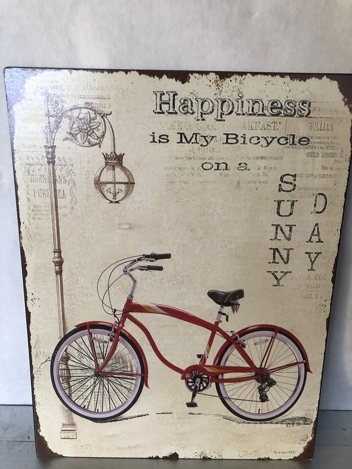 **Quadro decorativo in stile vintage con elegante raffigurazione di una bicicletta retrò rossa accompagnata dalla celebre frase "Happiness is My Bicycle on a Sunny Day", perfetto per donare un'atmosfera rilassata e nostalgica agli ambienti. La grafica effetto anticato, impreziosita da dettagli come il lampione d'epoca e la finitura vissuta, richiama il fascino delle vecchie insegne decorative e dello stile industriale. Ideale per arredare soggiorno, ingresso, cucina, studio, ufficio, taverna, bar, caffetter