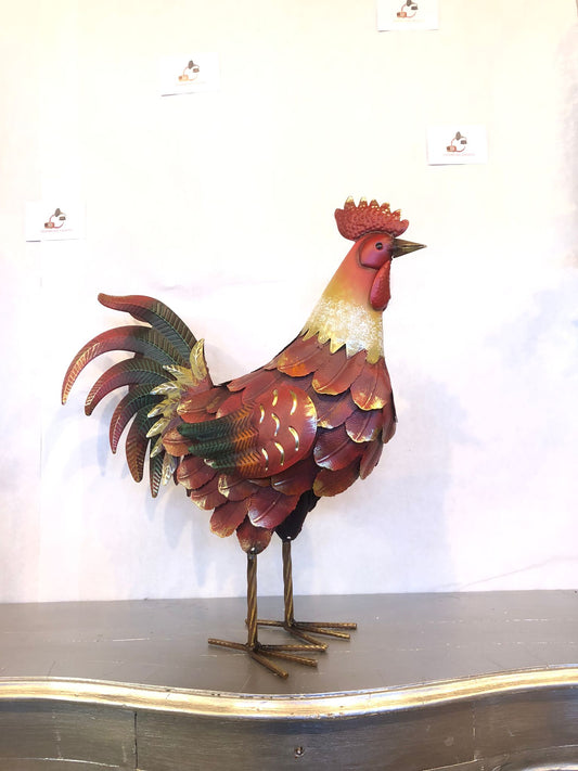 Gallo decorativo in metallo dipinto a mano, perfetto per arredare giardino, terrazzo, balcone, veranda, portico o ambienti interni in stile rustico e country. Realizzato interamente in metallo con lavorazione tridimensionale delle piume, si distingue per la coda finemente sagomata e la finitura anticata nei toni del rosso, rame, verde e oro, che dona un aspetto artigianale e di grande impatto estetico. La struttura autoportante assicura stabilità e permette di posizionarlo facilmente su qualsiasi superficie
