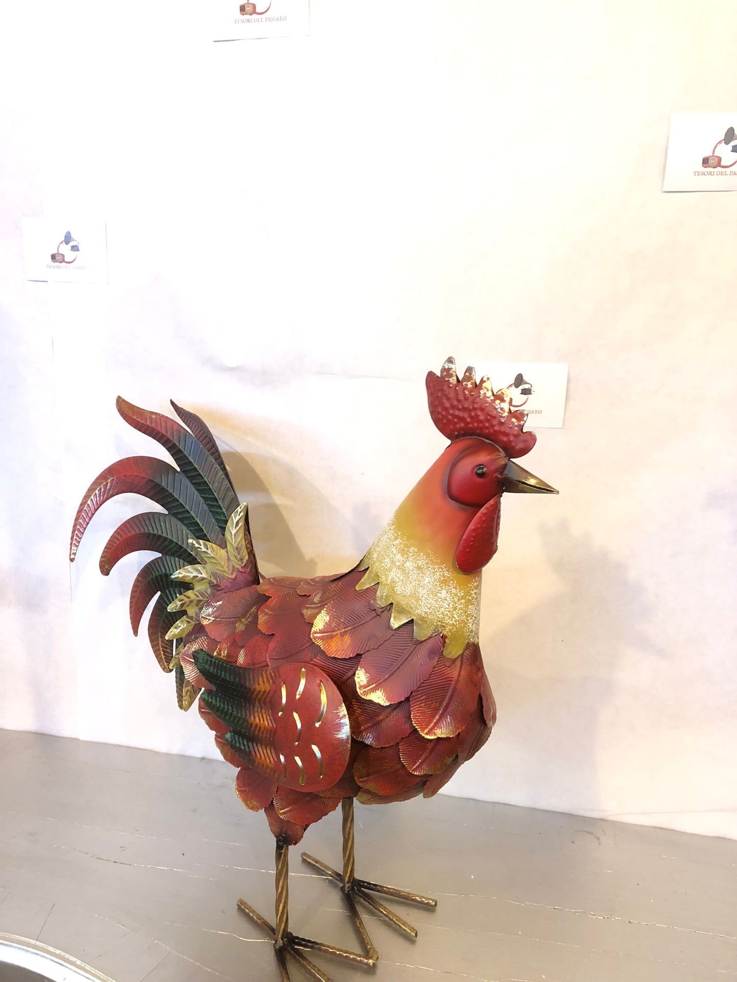 Gallo decorativo in metallo dipinto a mano, perfetto per arredare giardino, terrazzo, balcone, veranda, portico o ambienti interni in stile rustico e country. Realizzato interamente in metallo con lavorazione tridimensionale delle piume, si distingue per la coda finemente sagomata e la finitura anticata nei toni del rosso, rame, verde e oro, che dona un aspetto artigianale e di grande impatto estetico. La struttura autoportante assicura stabilità e permette di posizionarlo facilmente su qualsiasi superficie