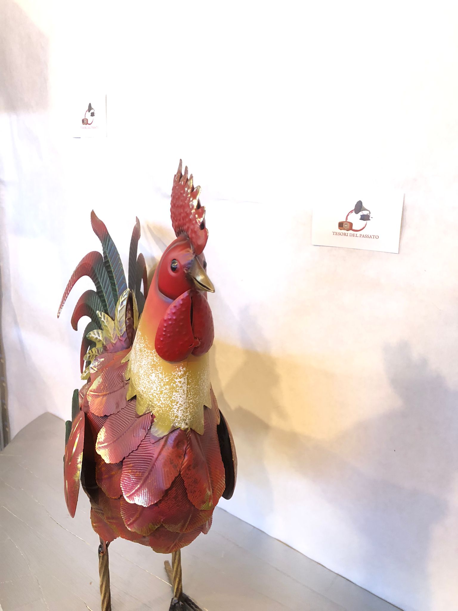 Gallo decorativo in metallo dipinto a mano, perfetto per arredare giardino, terrazzo, balcone, veranda, portico o ambienti interni in stile rustico e country. Realizzato interamente in metallo con lavorazione tridimensionale delle piume, si distingue per la coda finemente sagomata e la finitura anticata nei toni del rosso, rame, verde e oro, che dona un aspetto artigianale e di grande impatto estetico. La struttura autoportante assicura stabilità e permette di posizionarlo facilmente su qualsiasi superficie