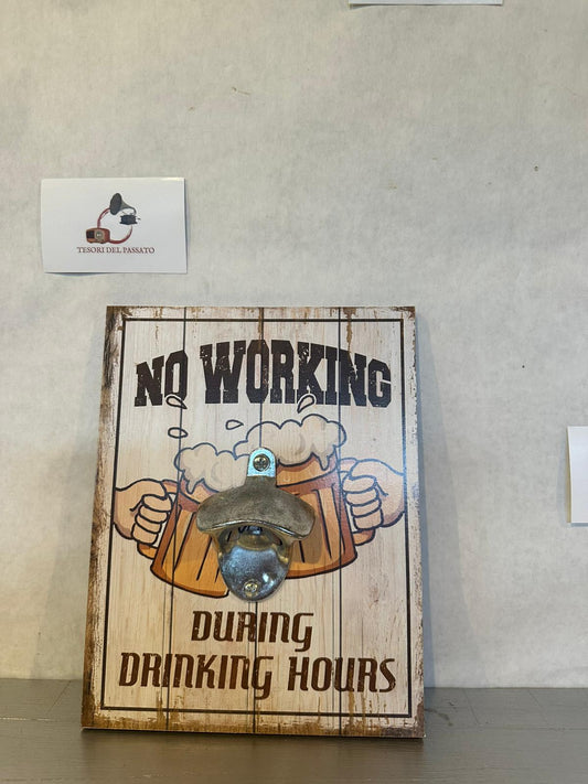 Apribottiglie da parete con stampa vintage "No Working During Drinking Hours", ideale per arredare cucina, taverna, pub, bar, cantina, garage o angolo birra con un simpatico stile retrò. Realizzato con robusta base in legno e apribottiglie in metallo fissato frontalmente, offre praticità e un design decorativo originale. La grafica effetto legno anticato raffigura due boccali di birra che brindano accompagnati dalla celebre scritta "No Working During Drinking Hours", perfetta per creare un'atmosfera convivi